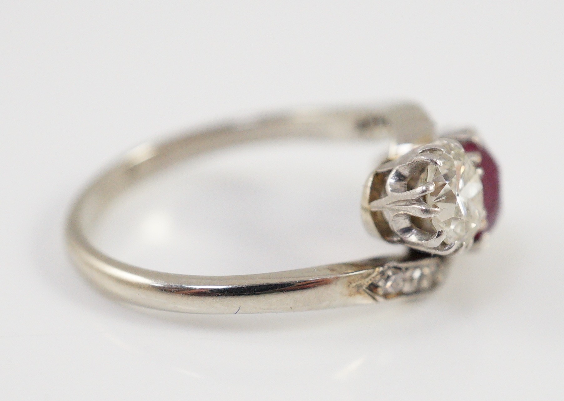 An 18ct white gold and platinum, two stone diamond and single stone synthetic? ruby set crossover ring, with diamond set shoulders